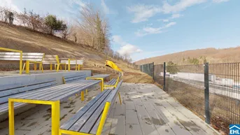 Außenbereich mit Sitzgelegenheiten, einem Spielplatz mit Rutsche und Blick auf die bewaldeten Hügel.