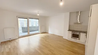 Heller Wohn- und Essbereich mit Parkettboden, integrierter Küchenzeile und Zugang zum Balkon.