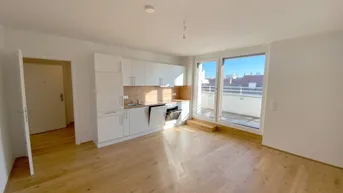 Helles Wohnzimmer mit integrierter Küche, Parkettboden und Zugang zu einem sonnigen Balkon.