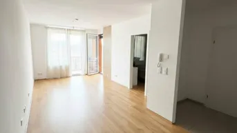 Helles, leeres Wohnzimmer mit Parkettboden und Zugang zu einem Balkon.