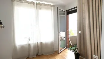 Helles Zimmer mit Holzboden, Holzwandverkleidung und Zugang zu einem Balkon.