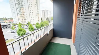 Balkon mit Blick auf die Stadt und umliegende Gebäude, ausgestattet mit Kunstrasen.