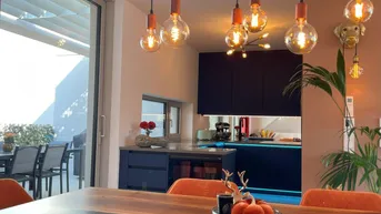 Moderner Essbereich mit Holztisch, orangefarbenen Stühlen und offener Küche, mit Zugang zur Terrasse.