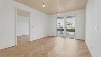 Helles, leeres Zimmer mit Fischgrätparkettboden, Holzbalkendecke und Zugang zu einem Balkon.