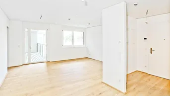 Helles, leeres Zimmer mit Holzboden, großen Fenstern und Zugang zu einem Balkon.