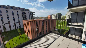 Blick von einem modernen Balkon mit Fliesenboden auf die umliegenden Gebäude und eine Grünfläche mit Spielplatz.