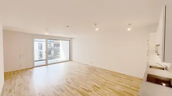 Helles, offenes Wohnzimmer mit integrierter Küchenzeile, Holzboden und Zugang zu einem Balkon.