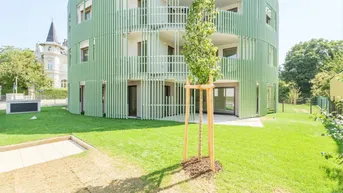 Modernes, rundes Gebäude mit grüner Fassade, umgeben von einer gepflegten Rasenfläche und jungen Bäumen.