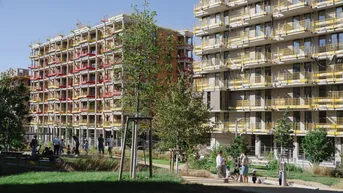 Neue Wohngebäude im Bau mit einer Grünfläche und spielenden Kindern im Vordergrund.
