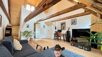 Gemütliches Wohnzimmer im Dachgeschoss mit Holzbalken, Holzdachschrägen und großem Sofa.