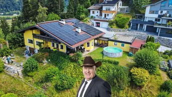 Luftaufnahme eines gelben Hauses mit Solaranlage auf dem Dach und umgeben von viel Grün.