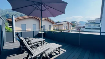 Sonniger Balkon mit Liegestühlen, Sonnenschirm und herrlichem Bergblick in die Natur.