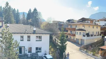 Panoramablick von einem Holzbalcon auf die umliegende Wohnsiedlung und ferne Berge.