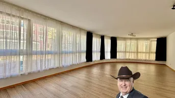 Geräumiges Wohnzimmer mit vielen Fenstern, hellem Laminatboden und weiß gestrichenen Wänden.