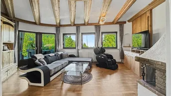 Geräumiges Wohnzimmer mit Holzbalkendecke, Kamin und großen Fenstern mit Blick ins Grüne.