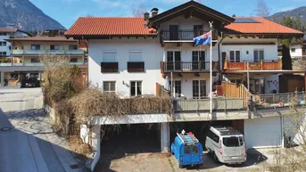 Mehrfamilienhaus mit mehreren Balkonen, Garagen und Bergblick in ländlicher Umgebung.