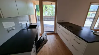 Moderne Küche mit Kochinsel, integriertem Backofen und direktem Zugang zu einer großen Holzterrasse.