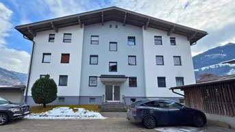 Modernes Mehrfamilienhaus mit heller Fassade und Satteldach, umgeben von winterlicher Berglandschaft.