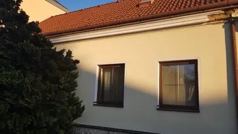 Fassade eines Hauses mit braunen Fenstern und einem roten Ziegeldach im Sonnenlicht.
