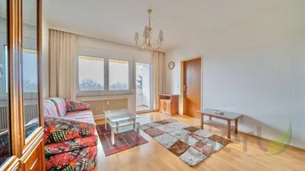 Helles Wohnzimmer mit Parkettboden, einem bunten Sofa und Zugang zum Balkon.