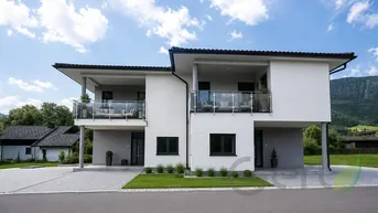 Moderne Doppelhaushälfte mit Balkonen und gepflegter Außenanlage unter blauem Himmel.