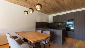 Moderne Küche mit dunklen Schränken, Holztisch und Holzbalkendecke.