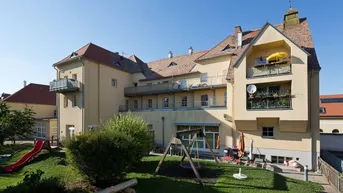 Großzügiger Außenbereich mit Spielplatz, Rasenfläche und Balkonen am historischen Gebäude.