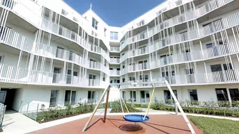 Moderner Neubau mit weißer Fassade und einem Spielplatz im Innenhof unter blauem Himmel.