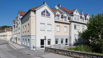 Mehrstöckiges Gebäude mit heller Fassade und Satteldach an einer Straße gelegen.