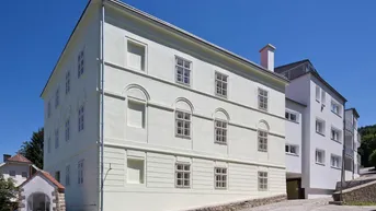 Historisches Gebäude mit heller Fassade und traditionellen Fenstern unter blauem Himmel.