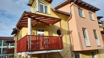 Moderne Fassade in Gelb und Rosa mit überdachtem Balkon und Sitzgelegenheiten im Freien.