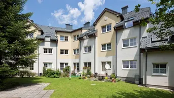 Blick auf die Rückseite des Mehrfamilienhauses mit gepflegtem Rasen und Sitzgelegenheiten im Gartenbereich.