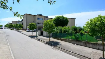 Mehrere moderne Wohngebäude entlang einer ruhigen Straße mit Bäumen und Grünflächen.