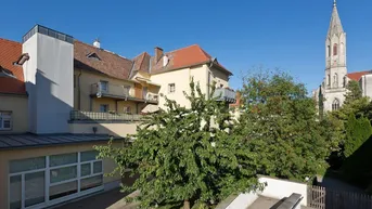 Gebäudeansicht mit umliegender Bebauung und Kirchturm im Hintergrund.