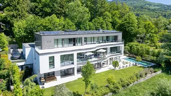 Moderne Villa mit mehreren Etagen, großen Glasfronten, Pool und Solaranlage, umgeben von üppigem Grün.