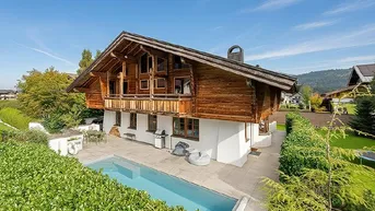 Traditionelles Chalet mit Außenpool, Bergblick und gepflegtem Garten unter blauem Himmel.