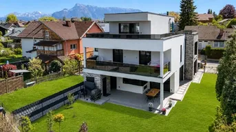 Modernes Wohnhaus mit Flachdach, großem Garten und Bergblick unter blauem Himmel.