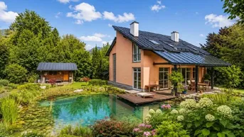 Großzügiges Einfamilienhaus mit Teich, Holzterrasse und weitläufigem Garten in grüner Umgebung.