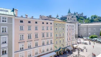 Panoramablick über einen historischen Stadtplatz mit Gebäuden und einer Burg im Hintergrund.