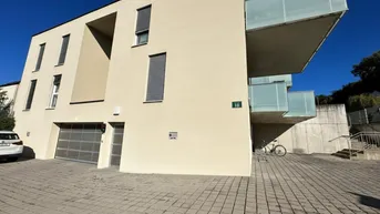 Moderne Architektur eines Neubaus mit hellbeiger Fassade, großen Balkonen und integrierter Tiefgarage.