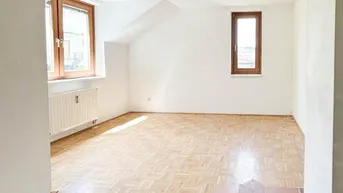 Geräumiger Wohnbereich mit Parkettboden und einem Bereich mit Terrakottafliesen, hell durch große Fenster.