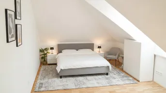 Helles Schlafzimmer im Dachgeschoss mit gemütlichem Bett, Teppich und Dachschräge.