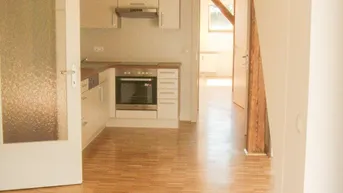 Helle Einbauküche mit Backofen und offenem Übergang zum Wohnbereich.