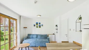Heller Wohn- und Essbereich mit Holzboden, blauem Sofa und direktem Zugang zum Garten.