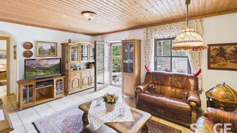 Gemütliches Wohnzimmer mit Holzdecke, Fliesenboden und Zugang zum Garten.