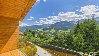 Geräumiger Balkon mit Holzverkleidung und Glasgeländer, bietet einen atemberaubenden Blick auf die Berge.