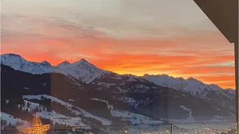 Spektakulärer Sonnenuntergang über den verschneiten Bergen, gesehen von einem Balkon mit festlicher Beleuchtung.