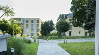 Moderne Wohngebäude in einer gepflegten Grünanlage mit Gehwegen und Bäumen.