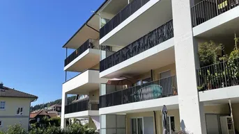 Modernes Mehrfamilienhaus mit mehreren Balkonen und gepflegter Außenanlage unter blauem Himmel.