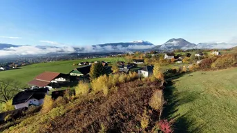 Weitläufige Landschaft mit Häusern, grünen Feldern und Bergen unter blauem Himmel.